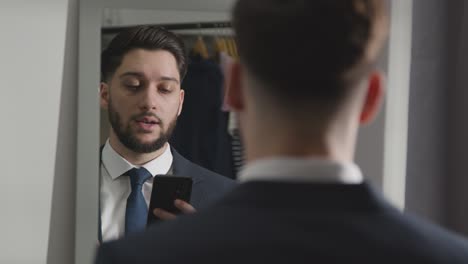 young man in suit at home practising job interview technique reflected in mirror using mobile phone