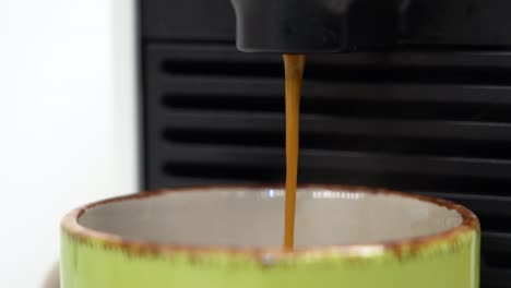 café caliente recién hecho que se vierte elegantemente en una taza verde de la máquina de café espresso en cámara lenta