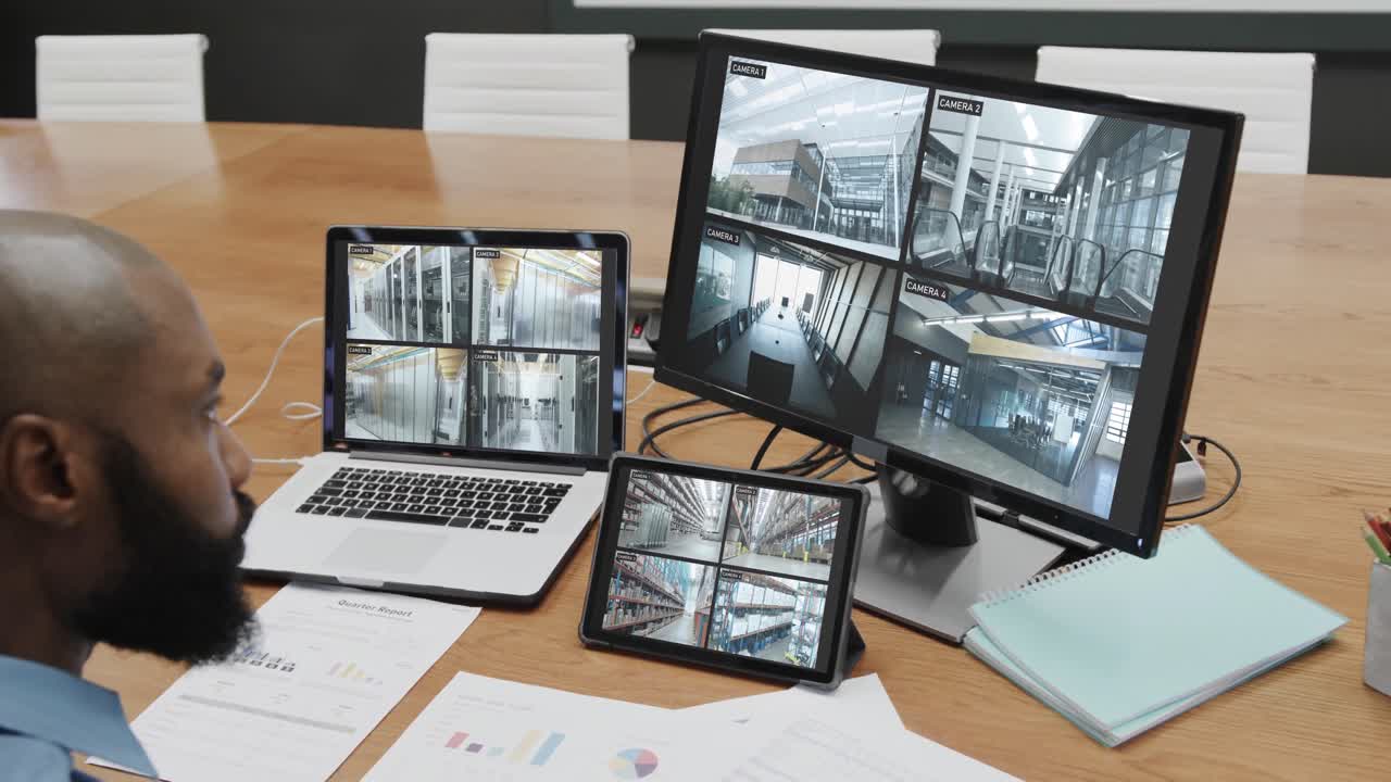 African american male security officer watching cctv camera views on computer screens, slow motion
