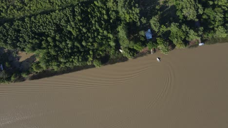 drone footage of small boat on brown water amazon river arriving home and making soft waves