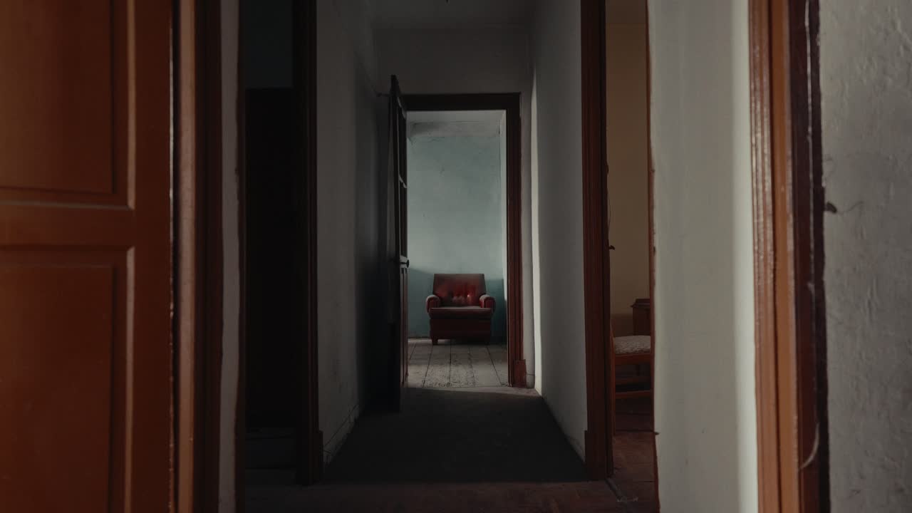 Long Dark Hallway Leading to an Empty Room with an Old Armchair