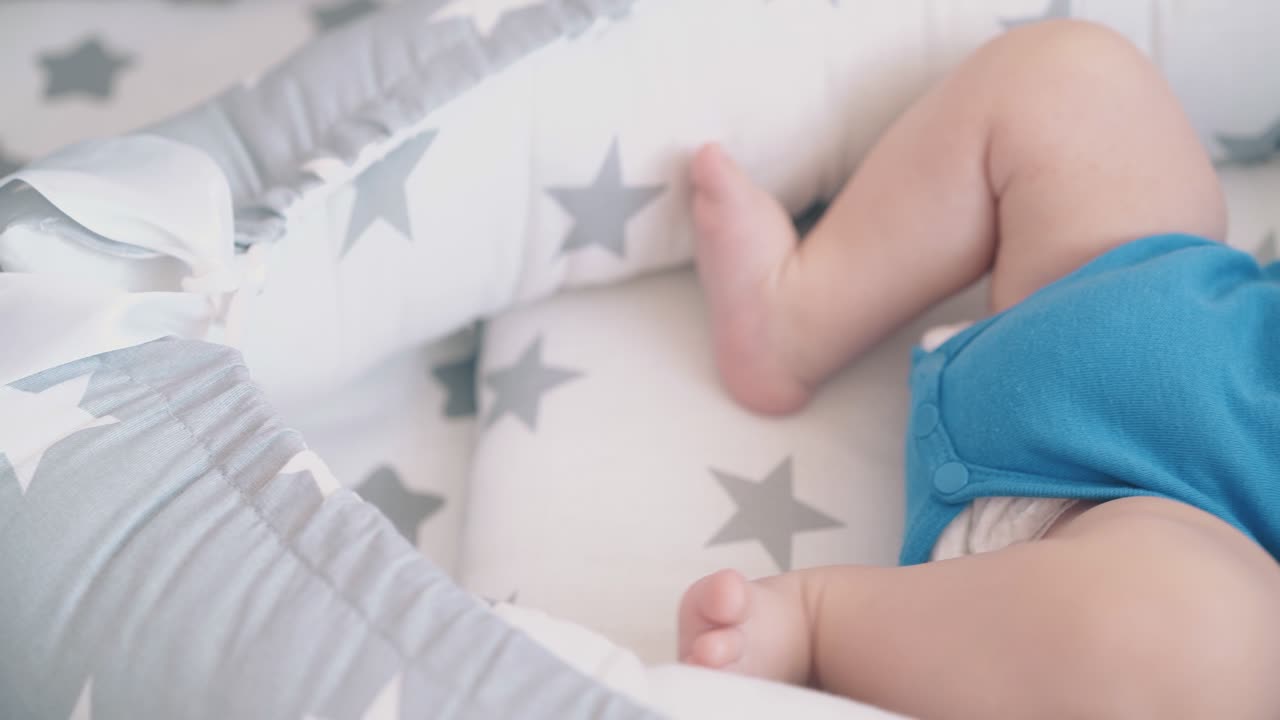 el niño pequeño patea las piernas desnudas chupando el muñeco en un capullo suave