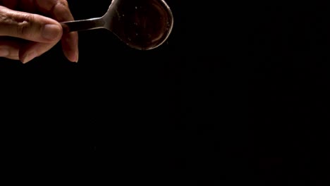 flour being poured off a tablespoon super slow motion on a black backdrop