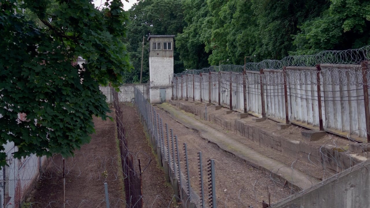 Prospettiva dall'alto che guarda lungo una zona di sicurezza fortificata con file di recinzioni di filo spinato e torre di osservazione delle guardie presso la prigione di Daugavpils in Lettonia