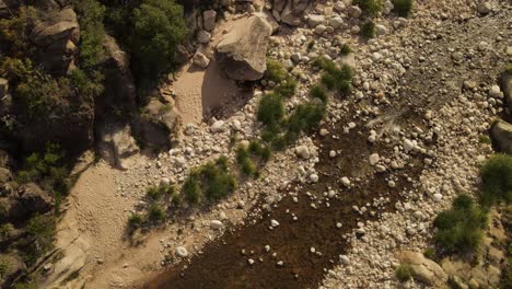 Toma-Aérea-De-Arriba-Hacia-Abajo-De-Una-Persona-Caminando-Por-Las-Rocas-Del-Río-Durante-El-Día-Soleado-En-El-Paisaje-Argentino