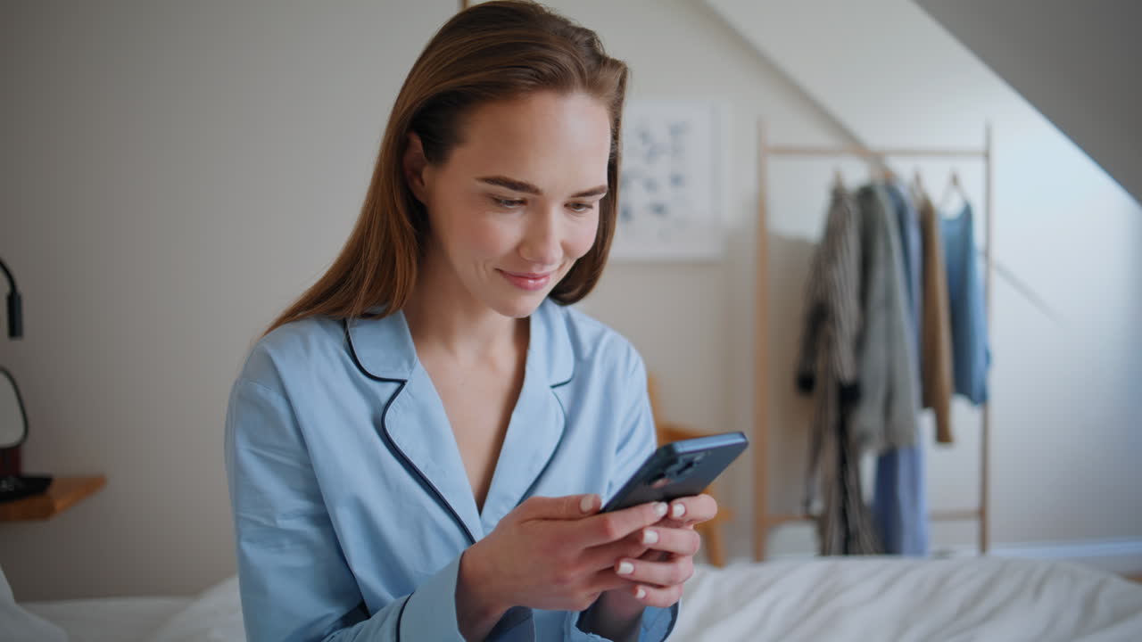 Joyful woman holding smartphone in cozy bed closeup. Student texting online