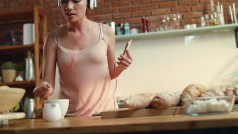 mujer joven sumergiendo azúcar en el café. niña bailando escuchando música en la cocina.