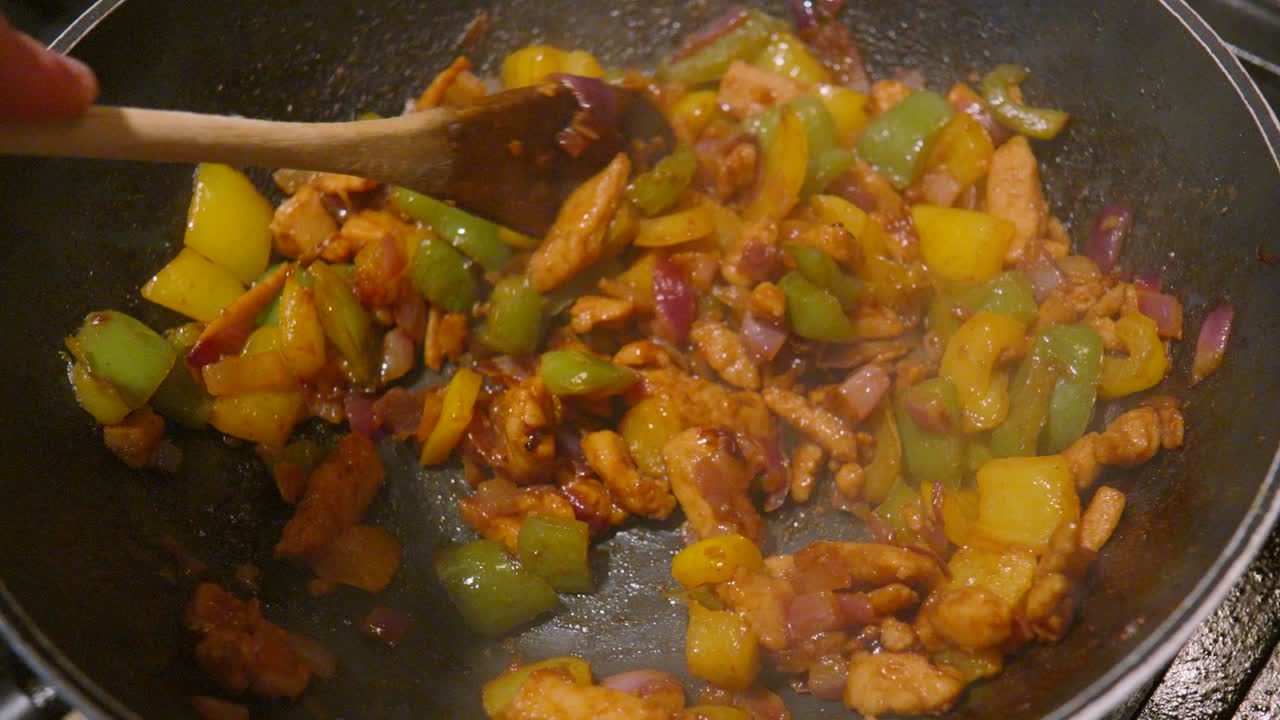 Slow Motion Stirring of Spicy Mexican Fajita Mix with Wooden Spoon with Hot Steam Rising as Dish Cooked on High Heat for Maximum Flavour.