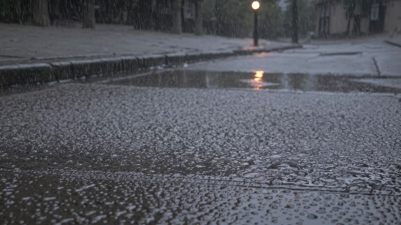Video girato dal basso di una strada bagnata dalla pioggia, che cattura riflessi e gocce di pioggia, creando un'atmosfera suggestiva