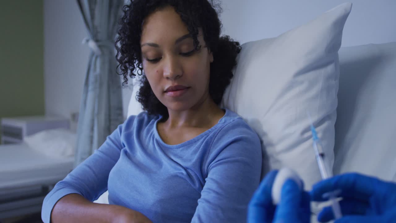 Paziente donna di etnia mista seduta nel letto d'ospedale che si prepara a ricevere un'iniezione.