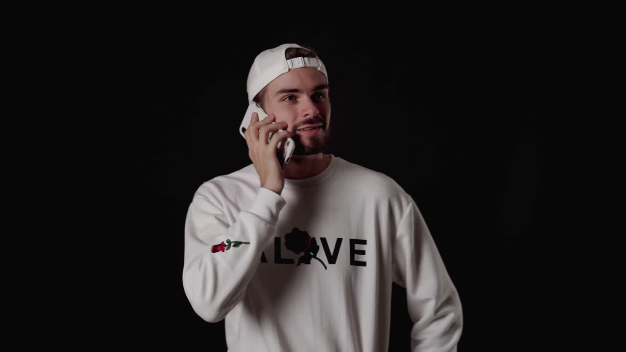 Uomo alla moda sui vent'anni che risponde eccitato al telefono cellulare, inquadratura ampia, sfondo nero.