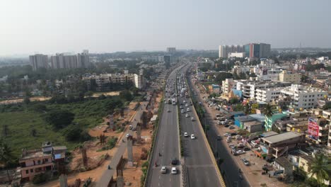 Indian-Highway-bridge-on-cinematic-aerial-footage-with-heavy-traffic-and-the-construction-of-a-metro-train-bridge-visible-above-the-service-road