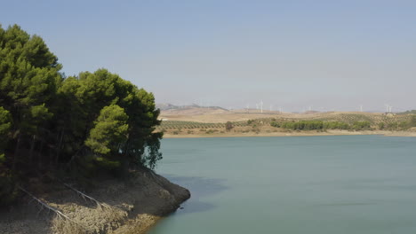 Windkraftanlagen-Jenseits-Einer-Insel-Mit-Bäumen,-See-Caminito-Del-Rey,-Spanien