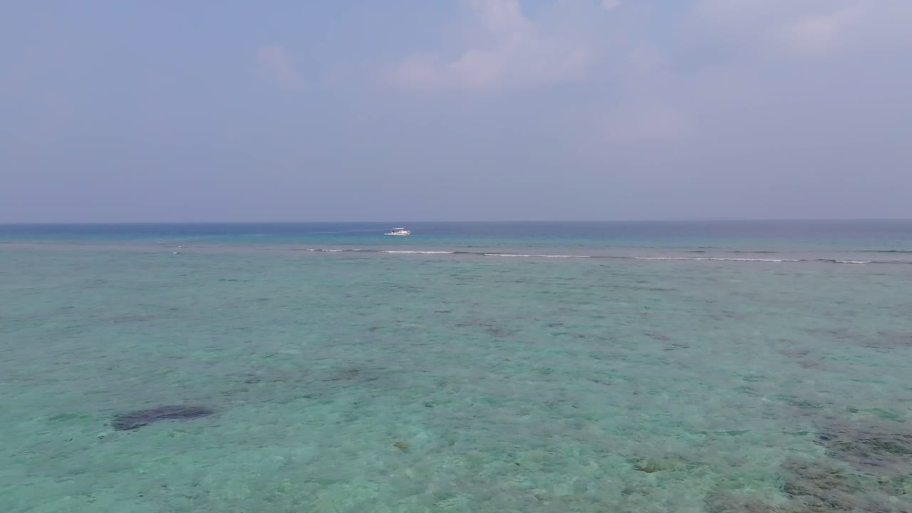 Impresionantes imágenes aéreas de dron volando desde la playa de la isla Vashafaru, a través del arrecife de coral y las aguas turquesas, hasta un barco de buceo en el norte de Maldivas.
