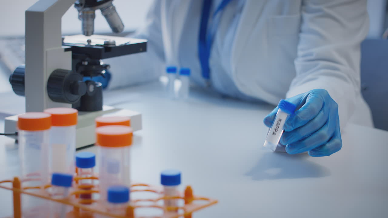 primer plano de un trabajador de laboratorio que lleva a cabo investigaciones utilizando un microscopio que sostiene un tubo de ensayo etiquetado kappa
