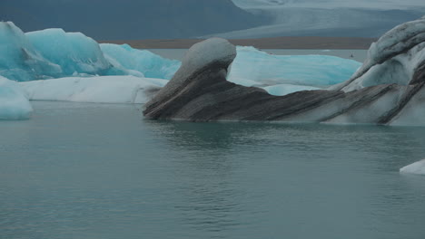 Glaciares-Flotando-En-Una-Laguna-Glaciar,-Islandia,-Con-Focas-Nadando-Y-Apareciendo-En-El-Agua,-Y-Gaviotas-Volando-Por-Encima,-Moviéndose-Hacia-La-Playa-De-Diamantes.