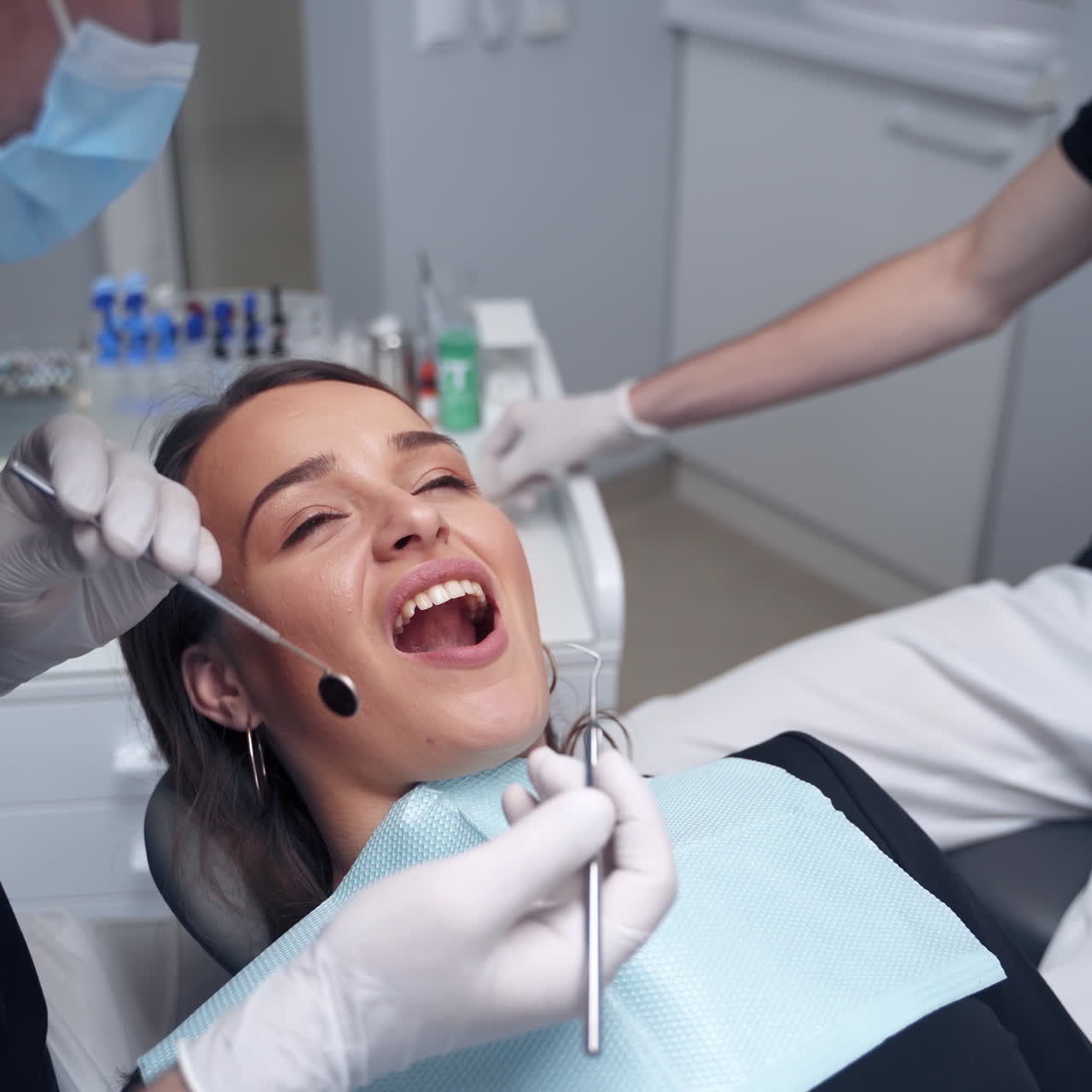 Dentist examines woman's teeth. Female's face with opened mouth in the dental chair. Specialist in mask treating patient's teeth with medical tools.