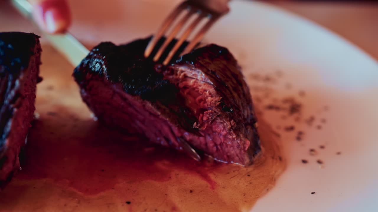 Close up of a knife slicing through a medium rare steak, exposing its tender, juicy interior
