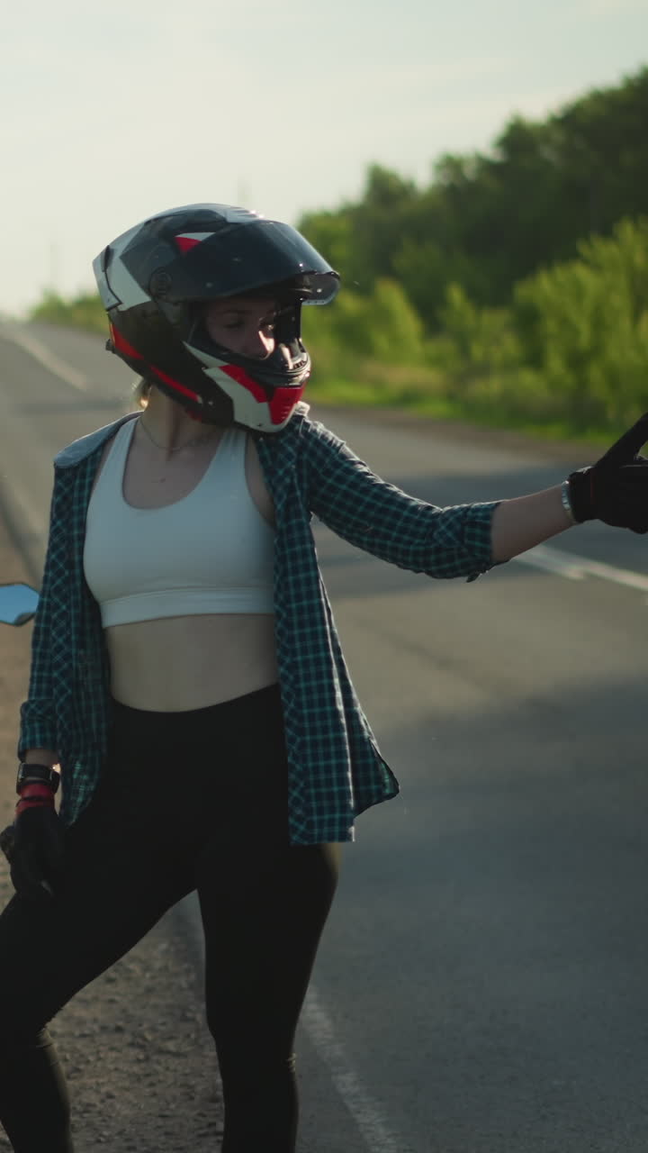dos mujeres con cascos están en una carretera cerca de la vegetación, una está sentada en una bicicleta deportiva roja mientras que la otra está de pie al lado de la bicicleta, dando un pulgar hacia arriba, un coche pasa en el fondo