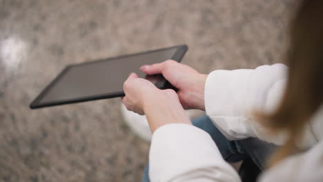 Close up of hands in white sleeve holding tablet while seated on granite floor, hands are gently swaying tablet, creating reflections on screen