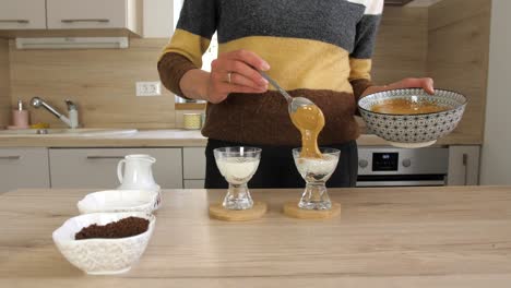 Woman-topping-hot-milk-with-dalgona-coffee-whipped-cream,-static-wide-shot