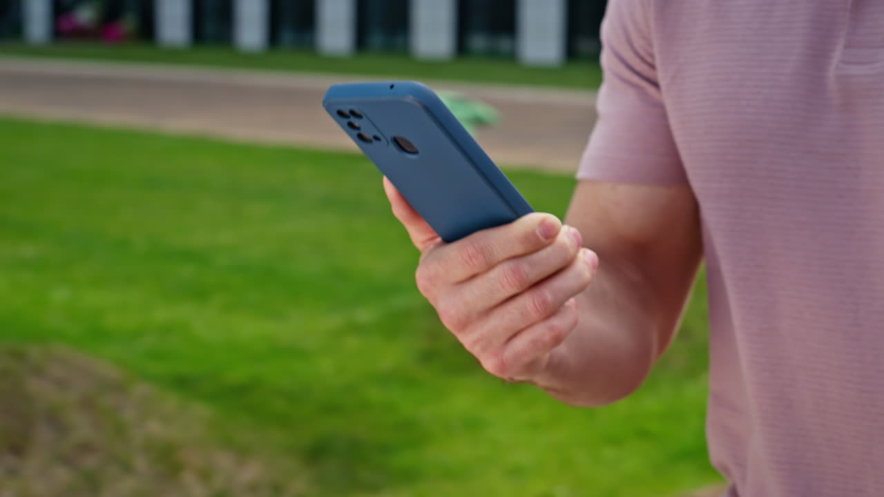 Strolling man answering message on smartphone at green town district closeup