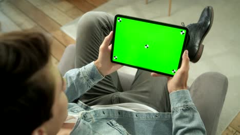 vista desde el hombro de un hombre sosteniendo y usando gestos con las manos en una pantalla de maqueta verde, una tableta digital sentada en una silla, un hombre comprando cosas o navegando por internet