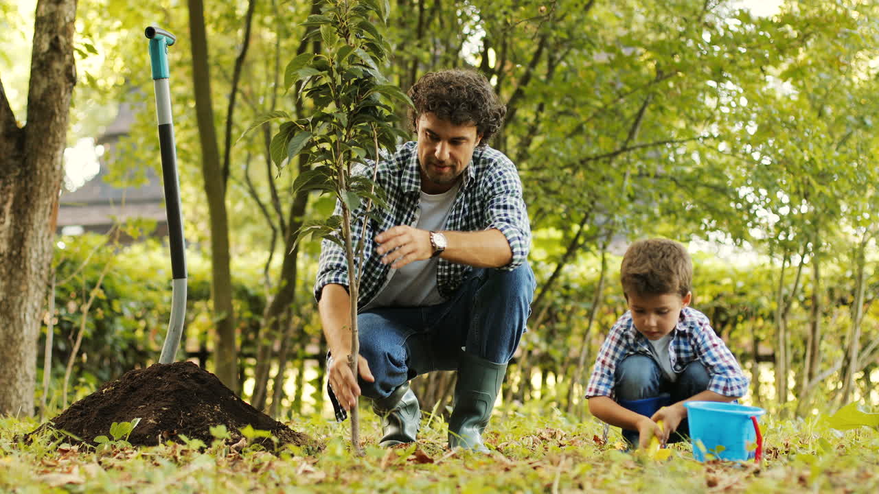 primer plano. retrato de un niño y su padre plantando un árbol. el padre pone la tierra en las raíces del árbol. el padre toca el árbol. fondo borroso