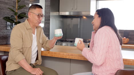 senior asian couple enjoying coffee together in cozy kitchen, sharing warm conversation