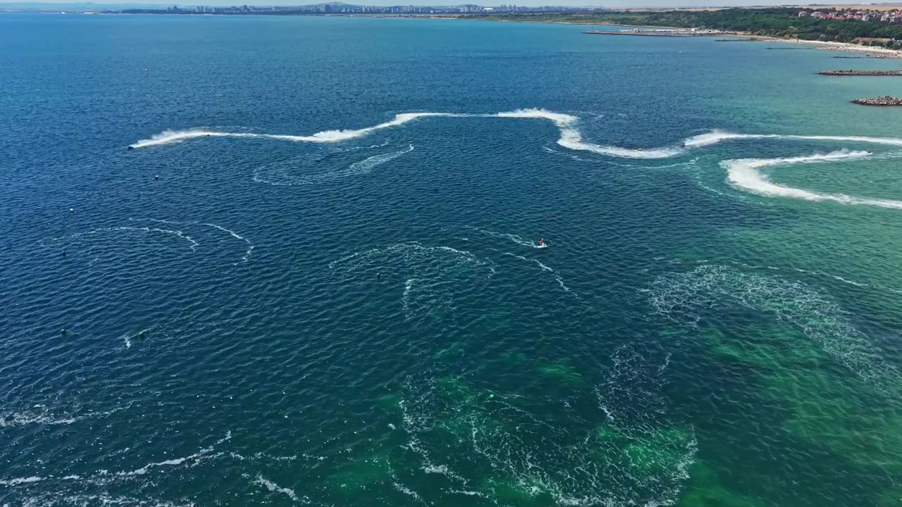 Jet ski racing takes place on blue water with waves and trails from jets around a coastal area