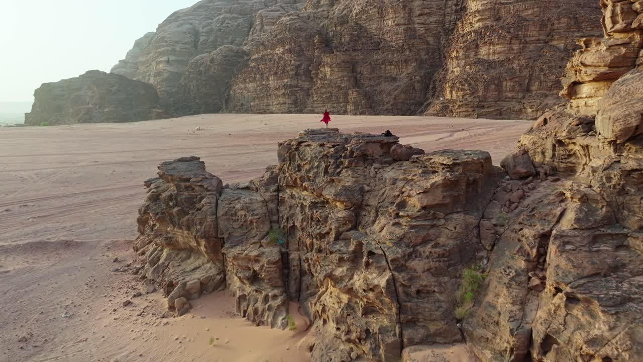 Donna in abito rosso in piedi su una scogliera rocciosa nel deserto del Wadi Rum
