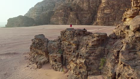 woman in red dress standing on rocky cliff in wadi rum desert