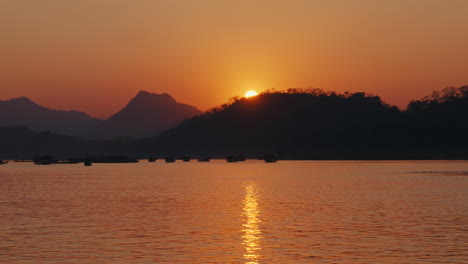 sunset over a river with mountains and boats