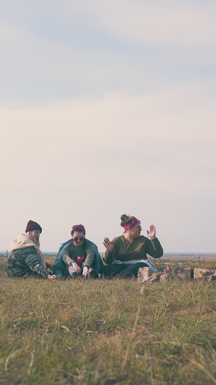 happy young women with hard drinks rest on grass at tent against clear sky in warm autumn evening low angle shot