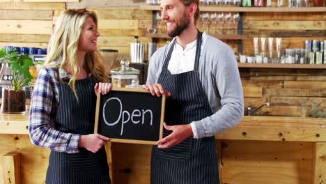 smiling waiter and waitresses holding open sign board