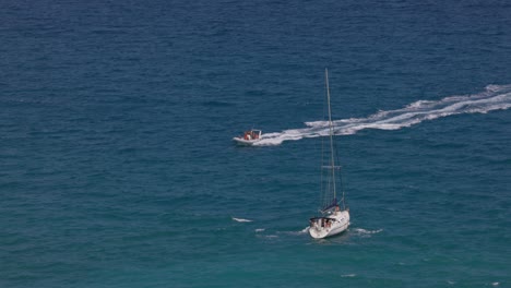 vela navegando y lancha rápida navegando dejando una estela blanca en la superficie azul del mar