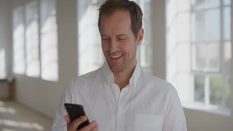 Retrato-De-Un-Joven-Feliz-Usando-Un-Teléfono-Inteligente-Sonriendo-Disfrutando-De-La-Comunicación-Por-Teléfono-Móvil-Enviando-Mensajes-De-Texto-Navegando-Por-La-Banca-En-Línea-Expresando-Satisfacción-Usando-Una-Camisa-Blanca