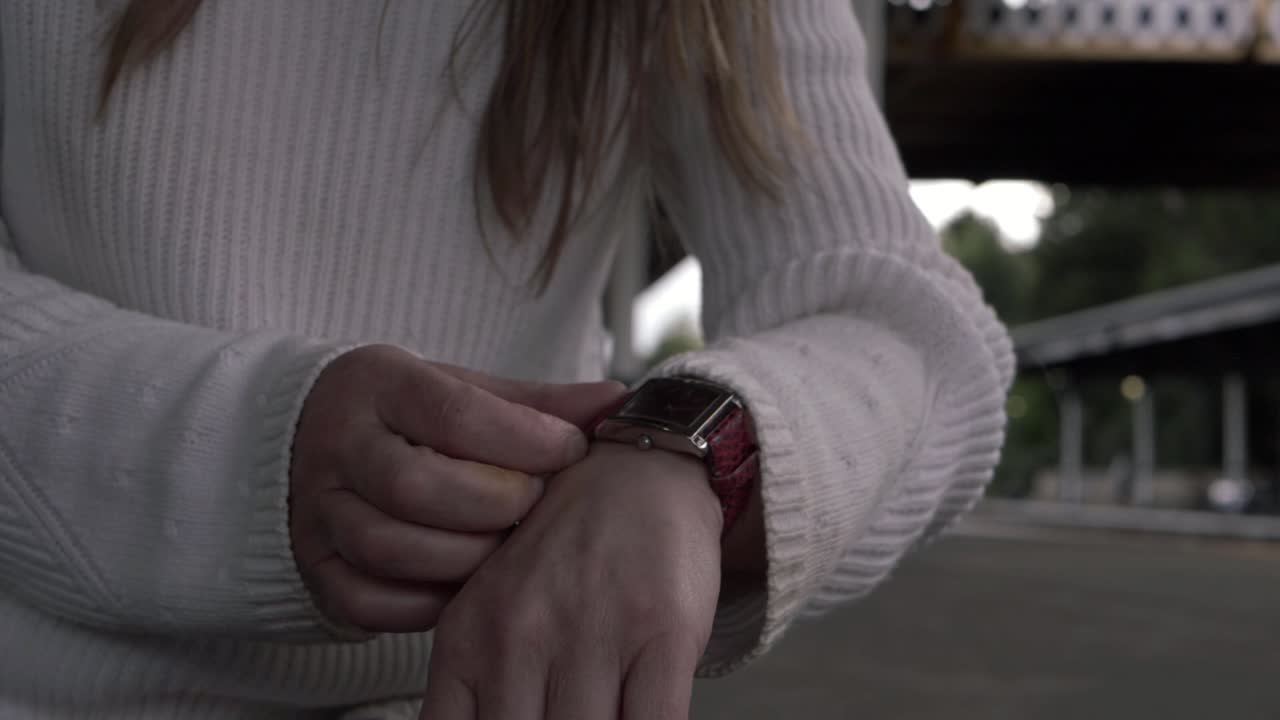Woman looking at wrist watch in train station medium shot