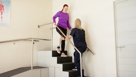 woman with prosthetic leg walking down stairs with therapist assisting her