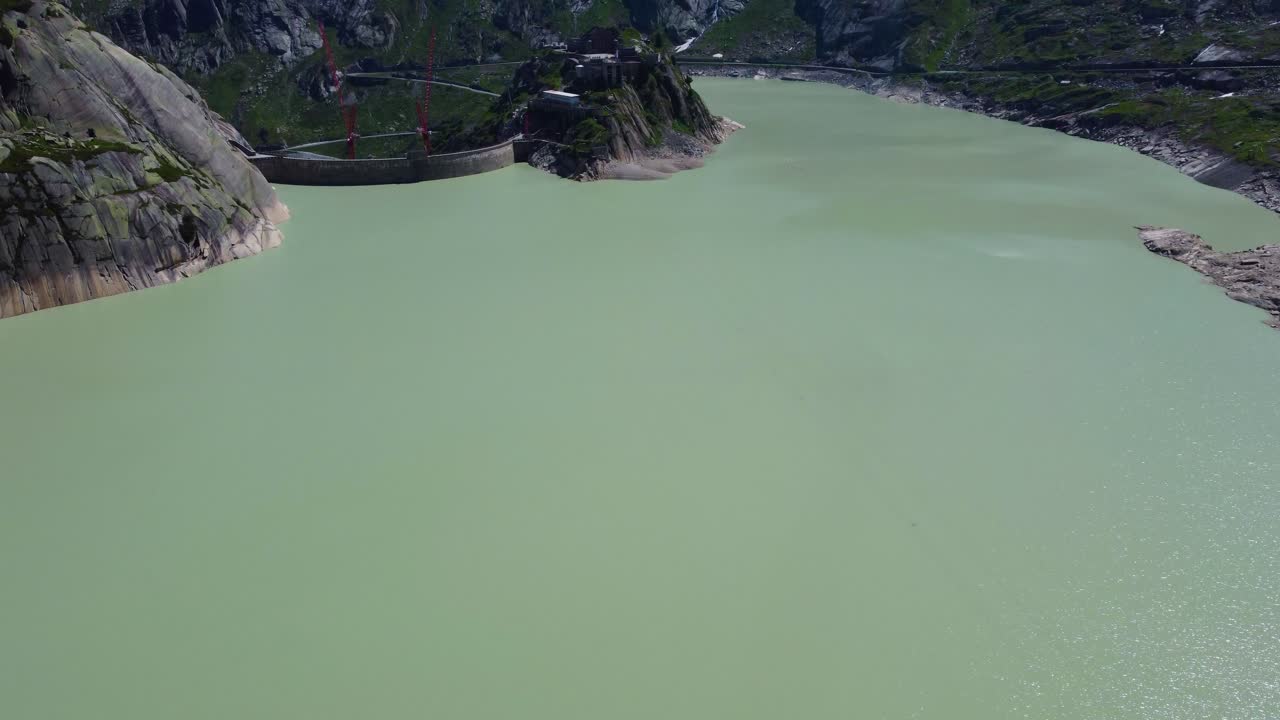 Aerial drone tilt up shot over Hotel Grimsel Hospiz beside a newly constructed dam close to Grimsel Pass along Swiss Mountain in Switzerland on a sunny day