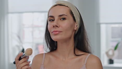 Satisfied-girl-powdering-face-using-brush-at-home-portrait.-Woman-posing-camera