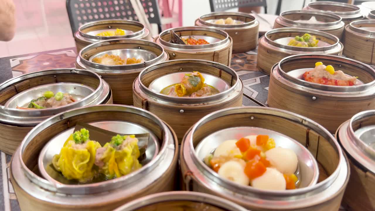 Hand uses spoon to serve dim sum onto plate from bamboo steamers in bright restaurant