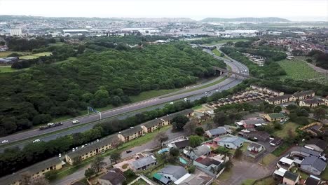 imágenes aéreas de un avión no tripulado volando sobre casas residenciales con vistas a una autopista concurrida con tráfico en movimiento en un suburbio de yellow wood park durban