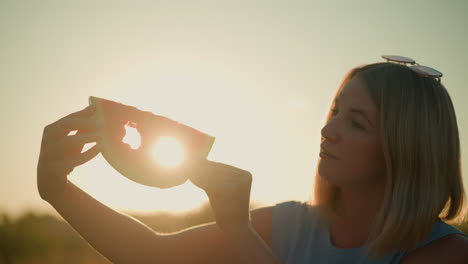 woman holding watermelon slice with star-shaped cutout against bright sunlight, creating a romantic and creative silhouette effect, illuminated fruit slice and sunlight together