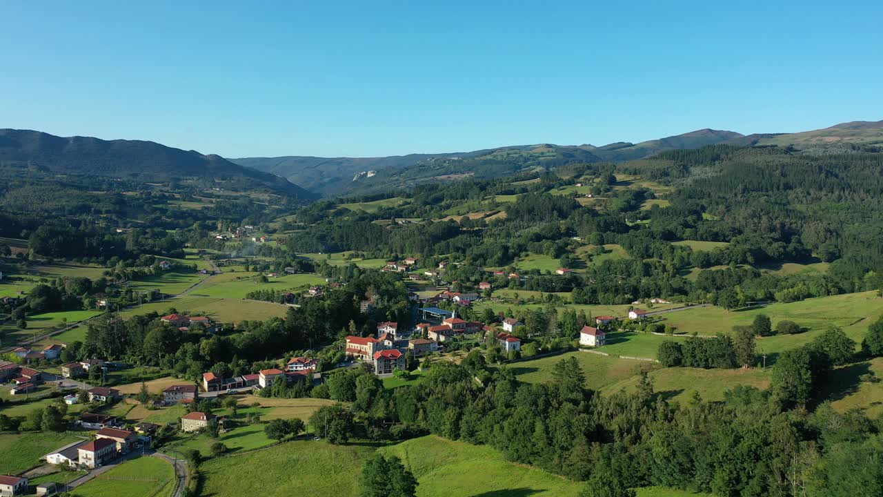 vuelo en el área vasco-cantabria sobre una ciudad rural con tierras de cultivo y exuberantes bosques de robles y montañas con su carretera y conducir en un atardecer con cielo azul en verano y hierba verde