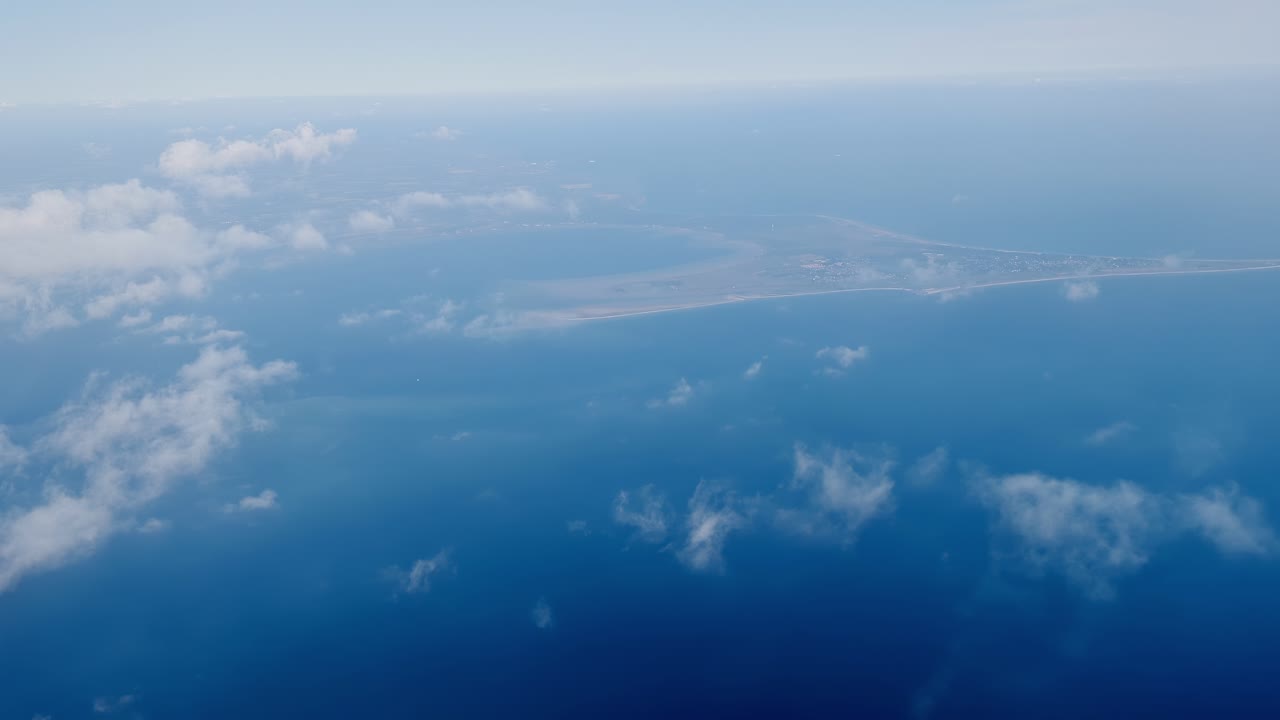aerial view dense white clouds over deep blue ocean subtle wave patterns visible through gaps vast open sea beneath sky light plays across water surface