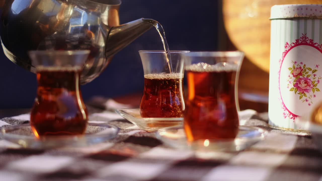 Black tea being poured into a traditional Turkish tea glass on checker table cloth