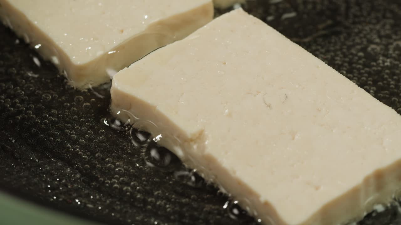 Fried tofu with sesame seeds and spices on cast iron pan, cooking japanese salad. Healthy ingredient for cooking vegan vegetarian diet food. Roasted tofu over black background.