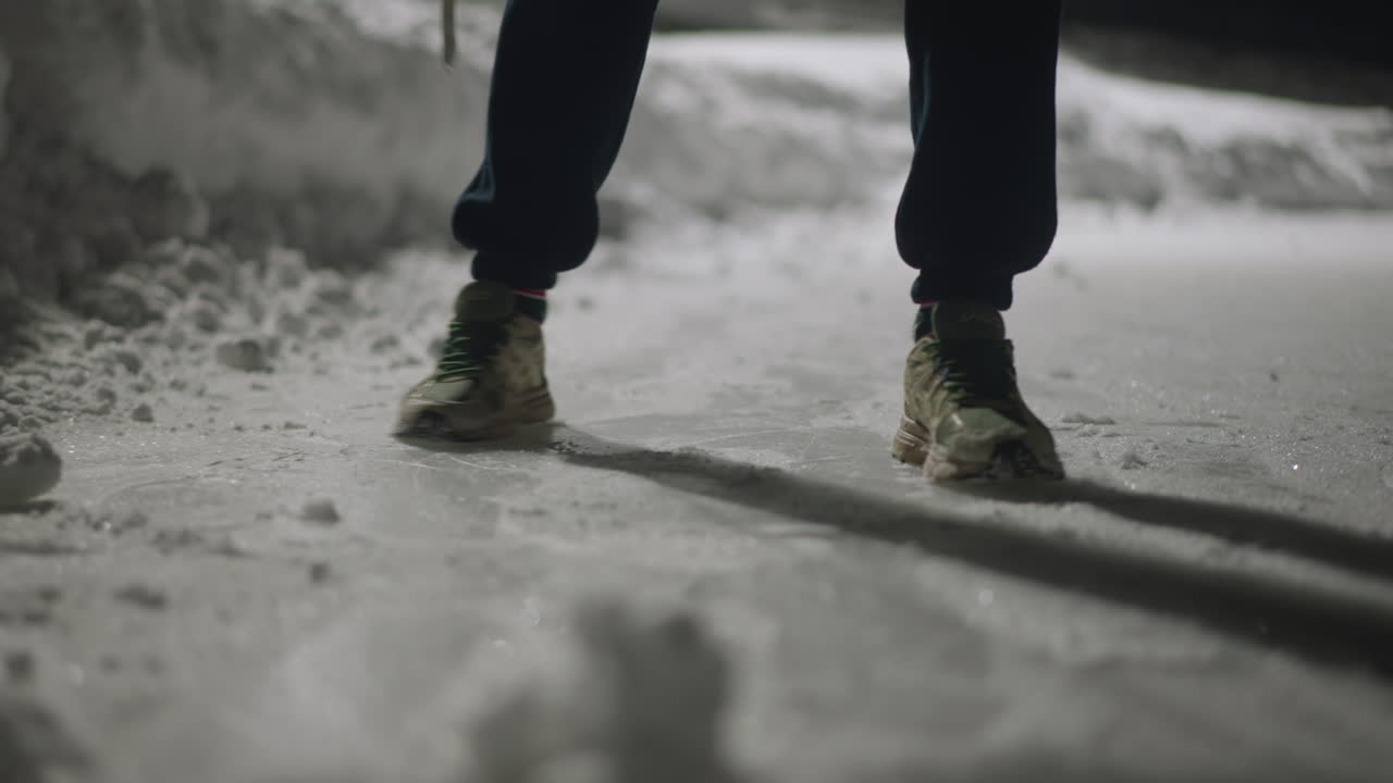 leg view of individual nearly slipping on icy snow covered ground while walking, then regaining balance and continuing movement, leaving visible footprints and casting elongated shadow