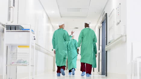 diverse male and female surgeons wearing surgical gowns walking in corridor at hospital, slow motion